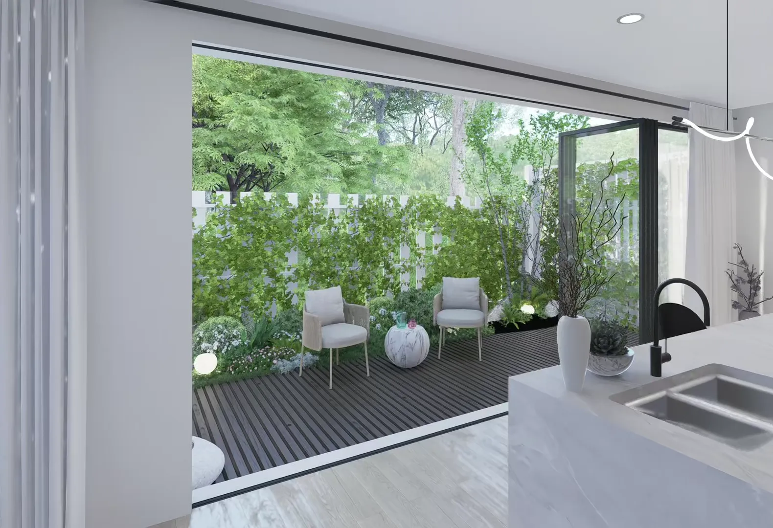 Full-height stacker doors folded open from a kitchen onto a decked courtyard, with lounge chairs, a hedged white picket fence and mature trees beyond.